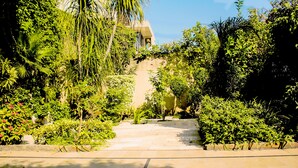 A stone pathway leading through a lush garden with dense foliage and a building in the background. - Lahore Guest House (Lahore)