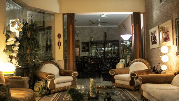 A living room with two brown armchairs, a glass coffee table, and a dining area in the background. - Lahore Guest House (Lahore)