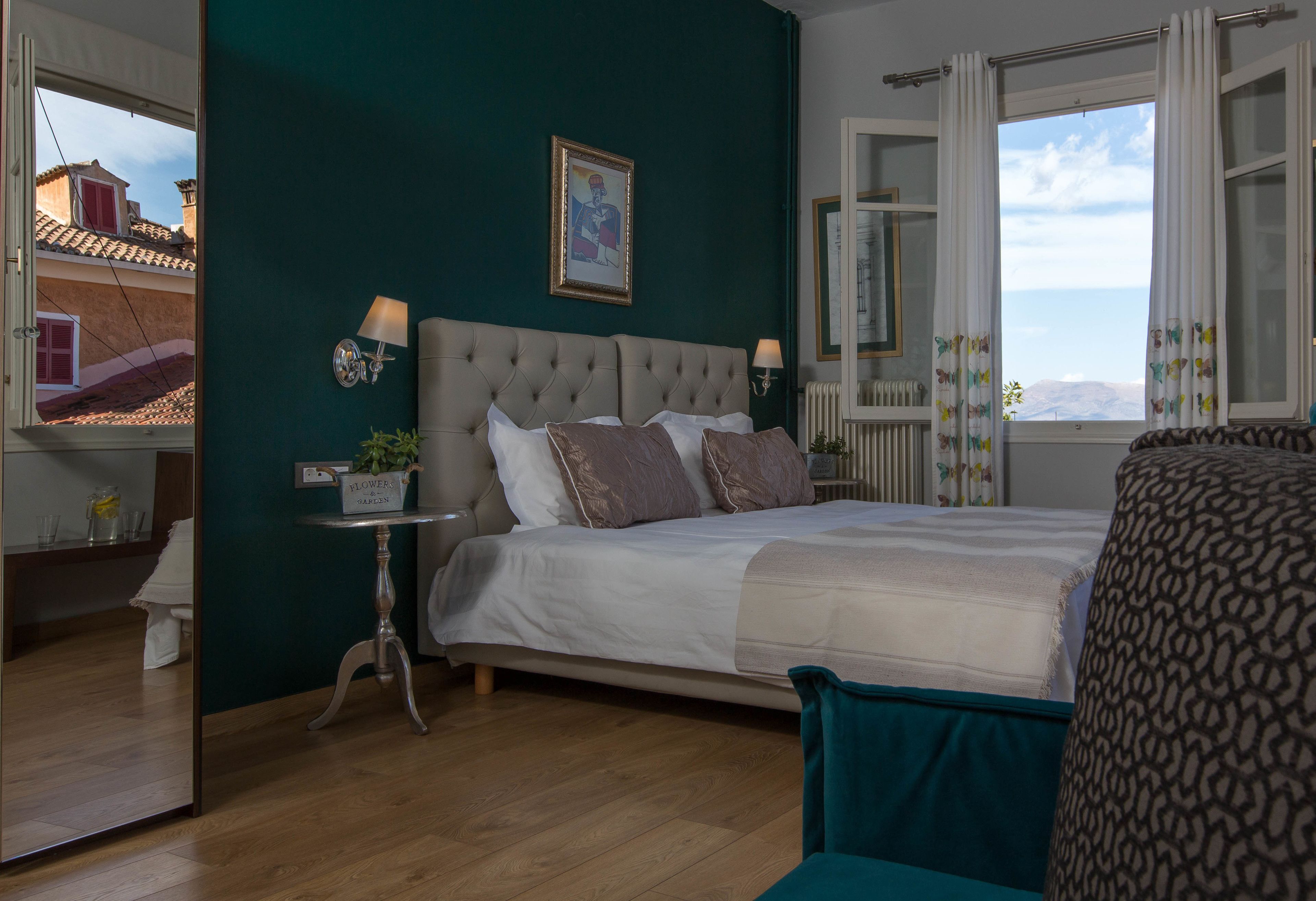 Une chambre à coucher avec un grand lit, une table de chevet avec une lampe, une fenêtre avec des rideaux et une vue sur les bâtiments à l’extérieur.