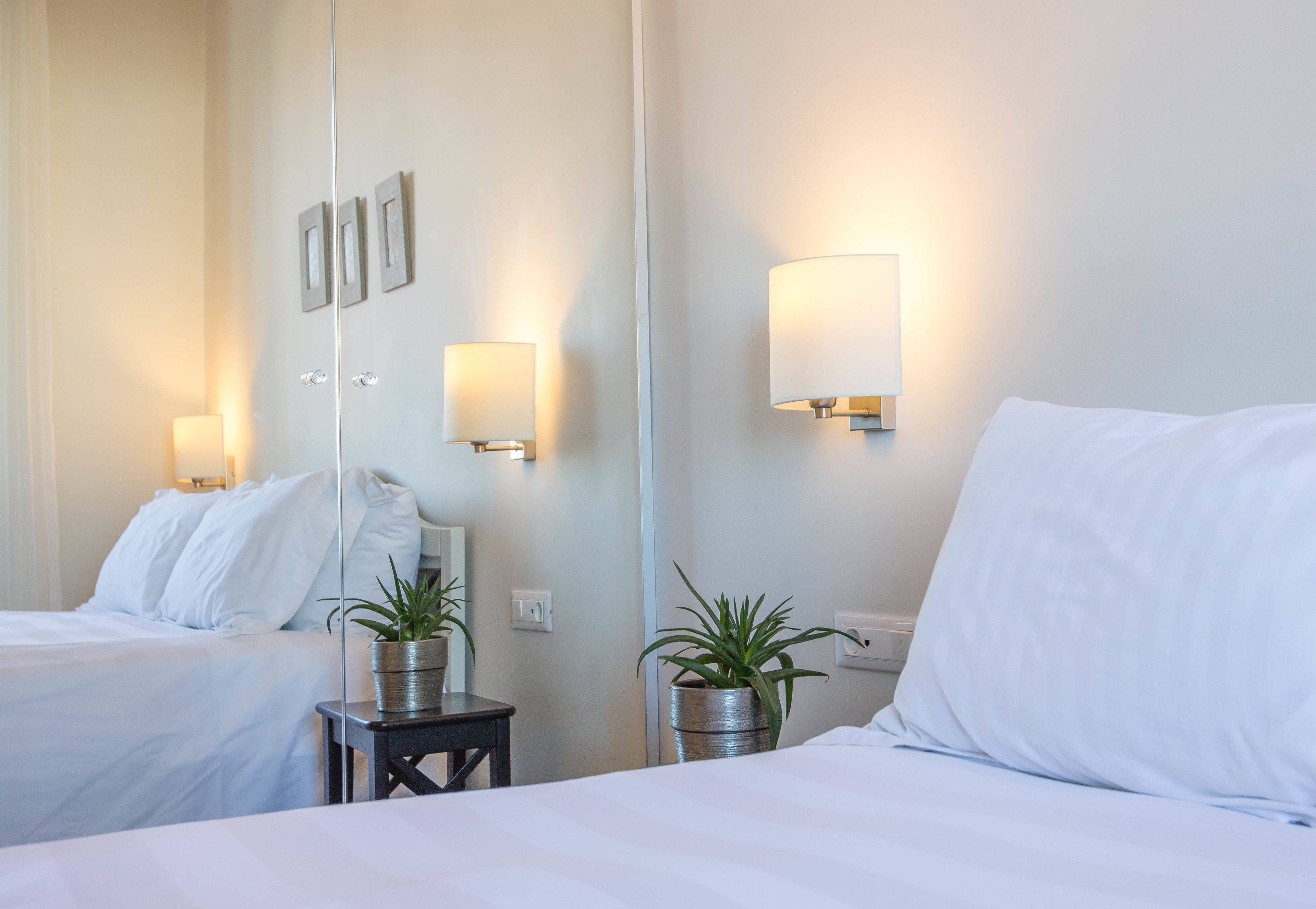 Habitación de hotel con dos camas, lámparas de noche, una mesita con una planta y un espejo en la pared.