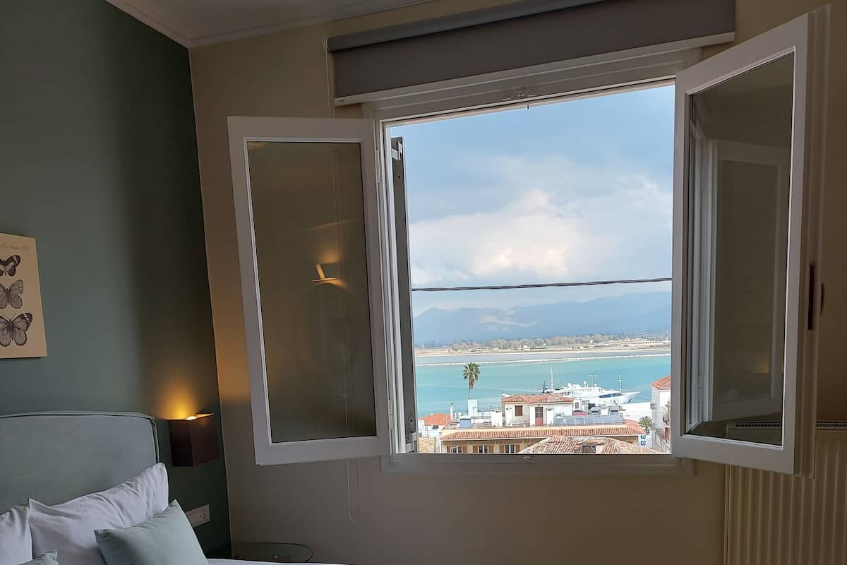 A bedroom with a bed, a bench, and a window with a view of a coastal area.