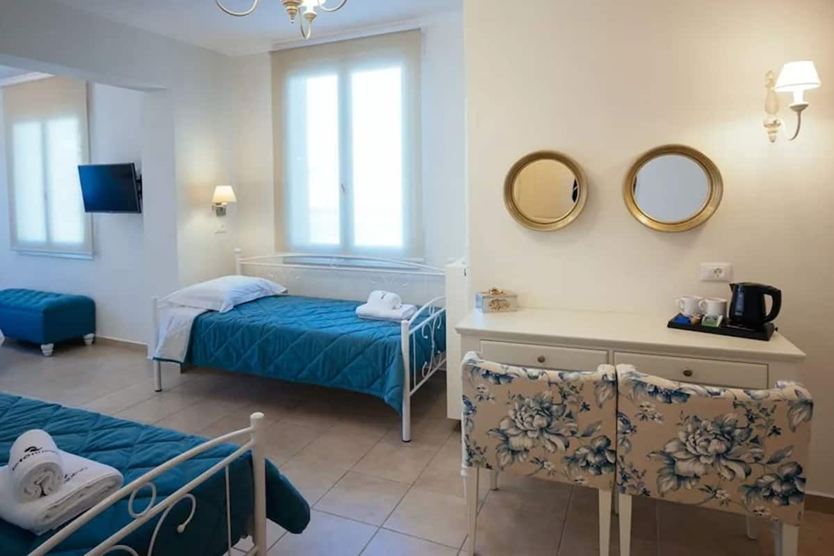A hotel room with two single beds, a desk with a chair, a TV, and a window with blinds.