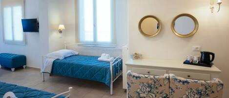 A hotel room with two single beds, a desk with a chair, a TV, and a window with blinds.