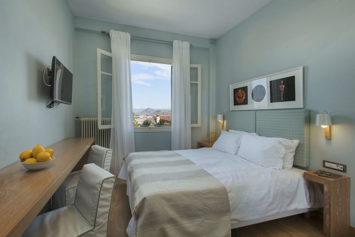 A hotel room with a bed, a desk with a bowl of lemons, a TV, and a window with curtains.