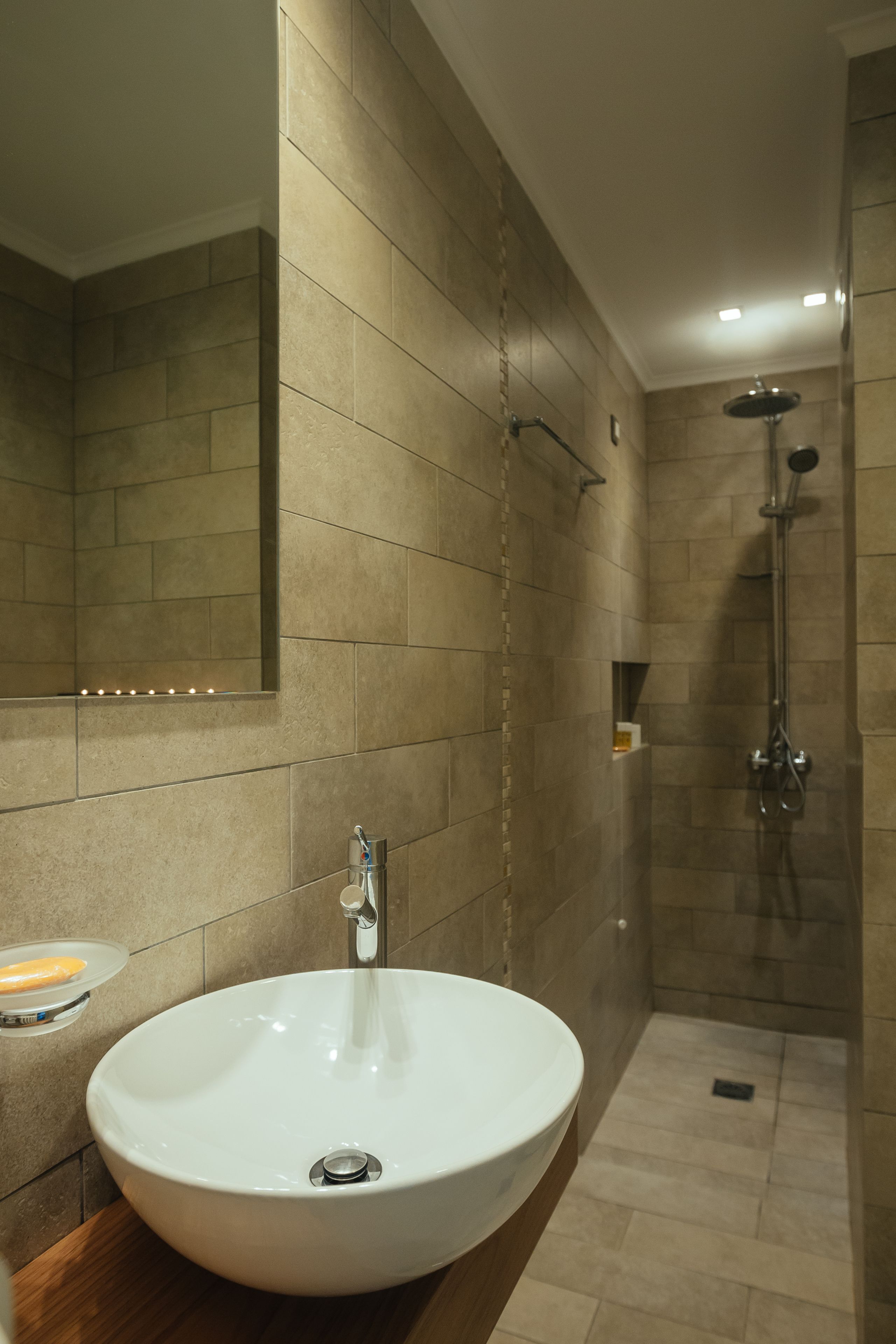 A modern bathroom with a large sink, a mirror, and a shower area.