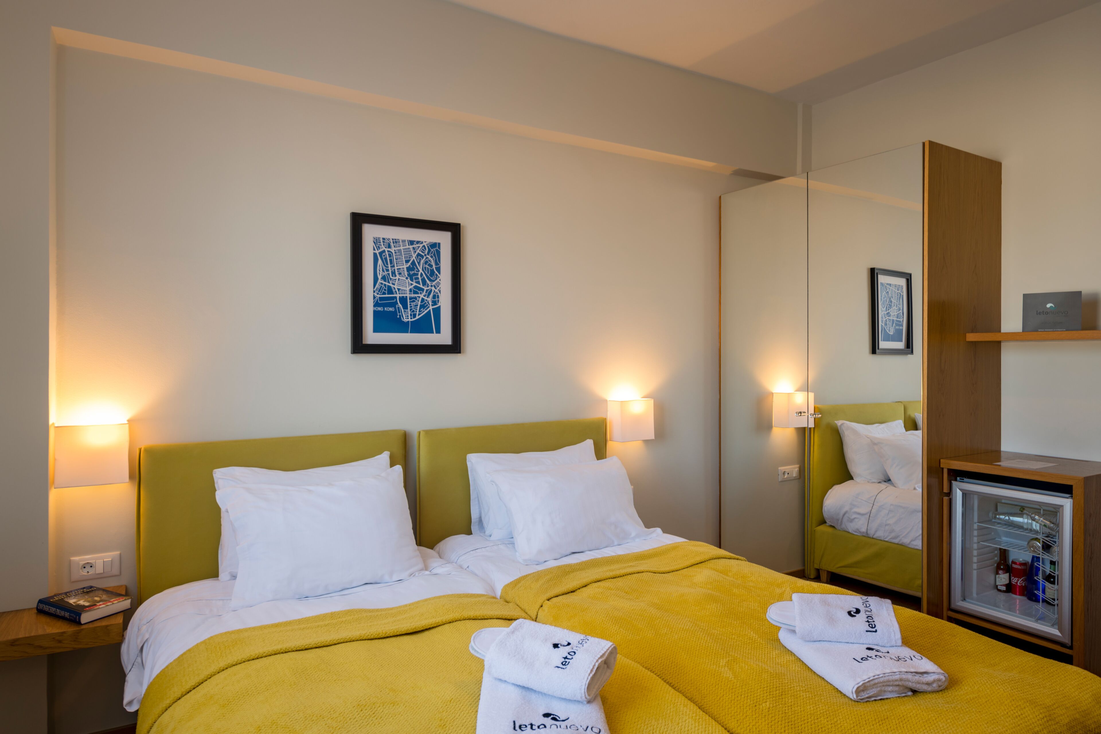 Camera d'albergo con un letto, due comodini, uno specchio, una lampada a parete e un minibar.