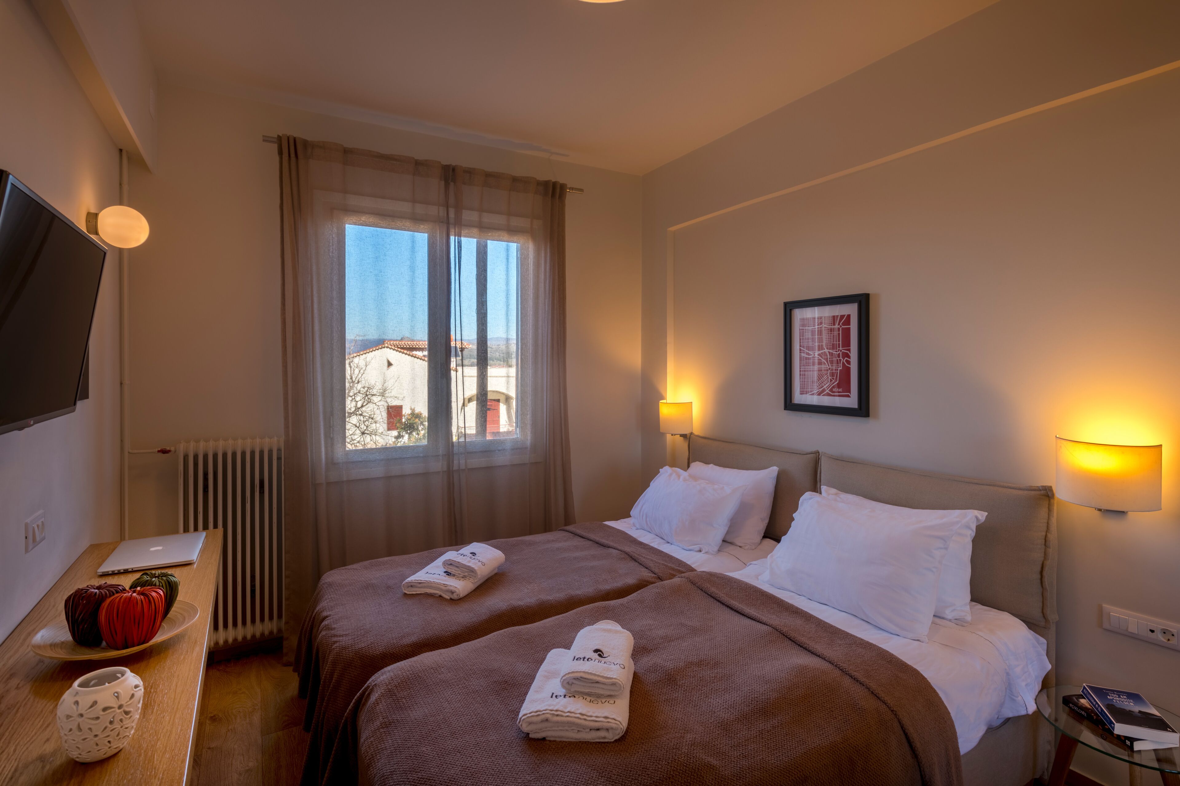 Une chambre d’hôtel avec deux lits, un bureau avec un ordinateur portable, une télévision et une fenêtre donnant sur des immeubles.