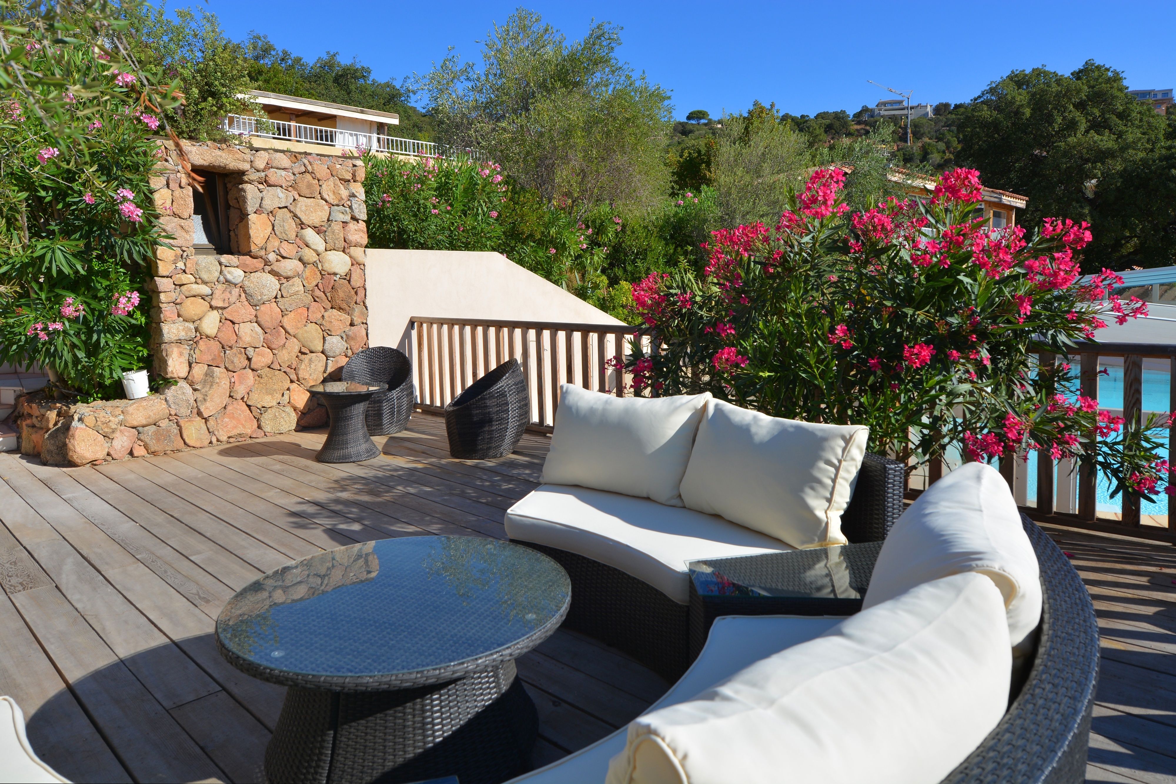 A wooden deck with outdoor furniture, a stone wall, and blooming pink flowers.