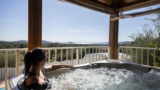 A person in a hot tub with a view of mountains and a white picket fence. - Résidence Chiar' Di Luna (Zonza)