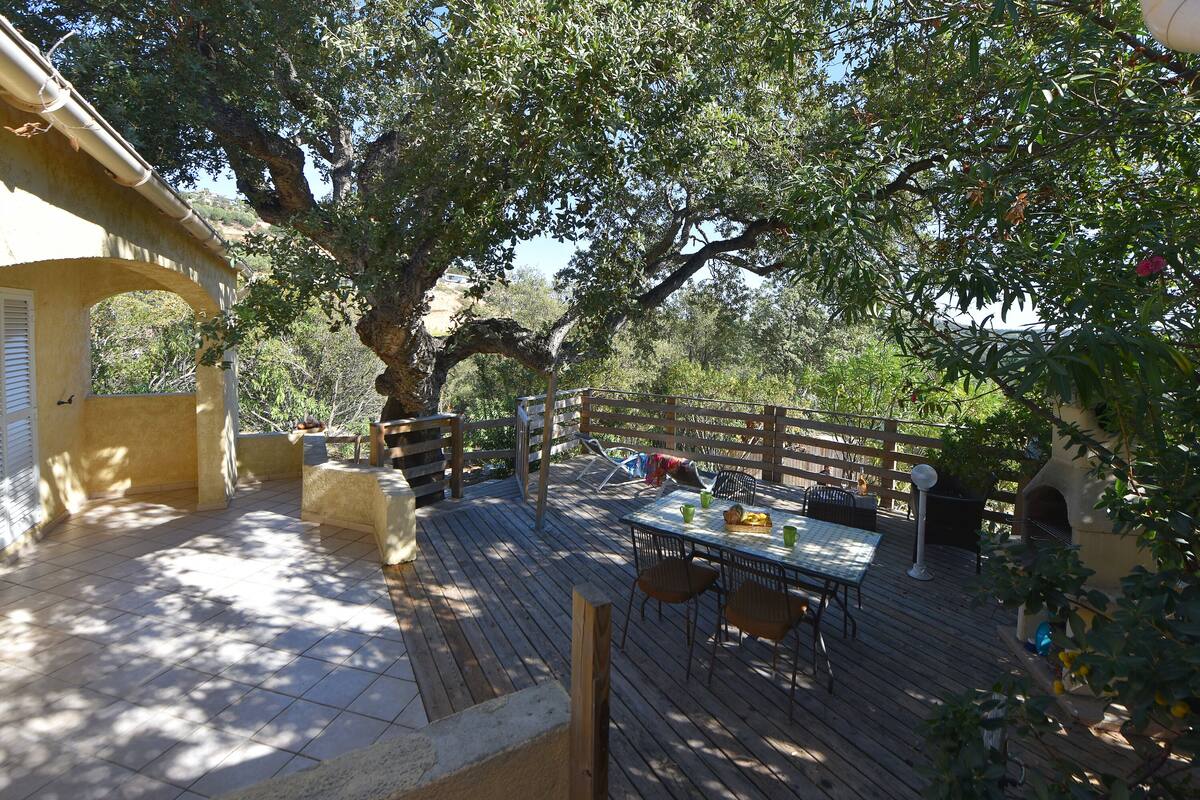 A wooden deck with a table and chairs, surrounded by trees and a pergola.