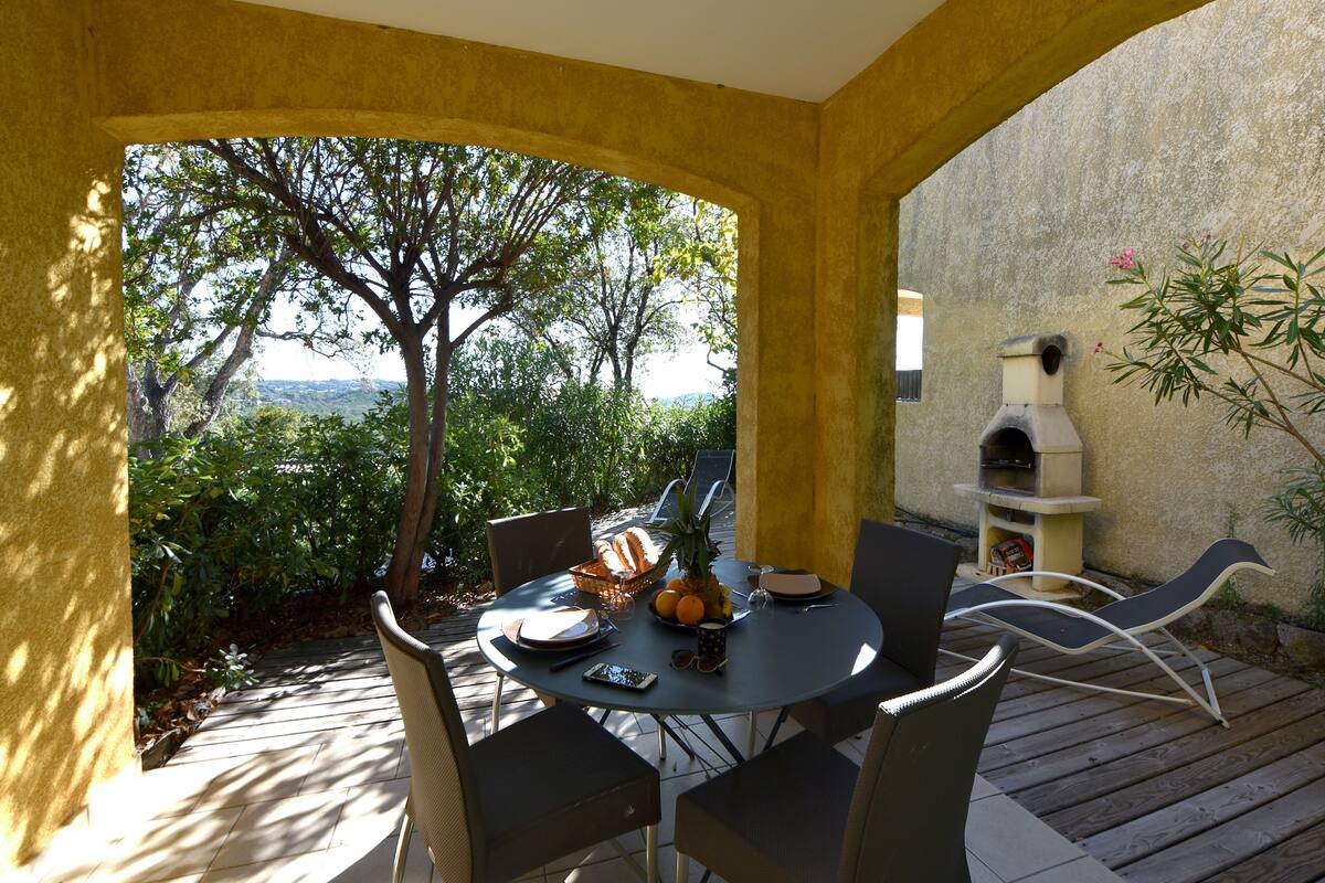 An outdoor dining area with a table set for two, surrounded by chairs, a basket of bread, and a bowl of fruit.