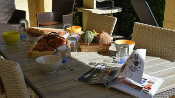 An outdoor dining area with wicker chairs, a table set with food, drinks, and a magazine.