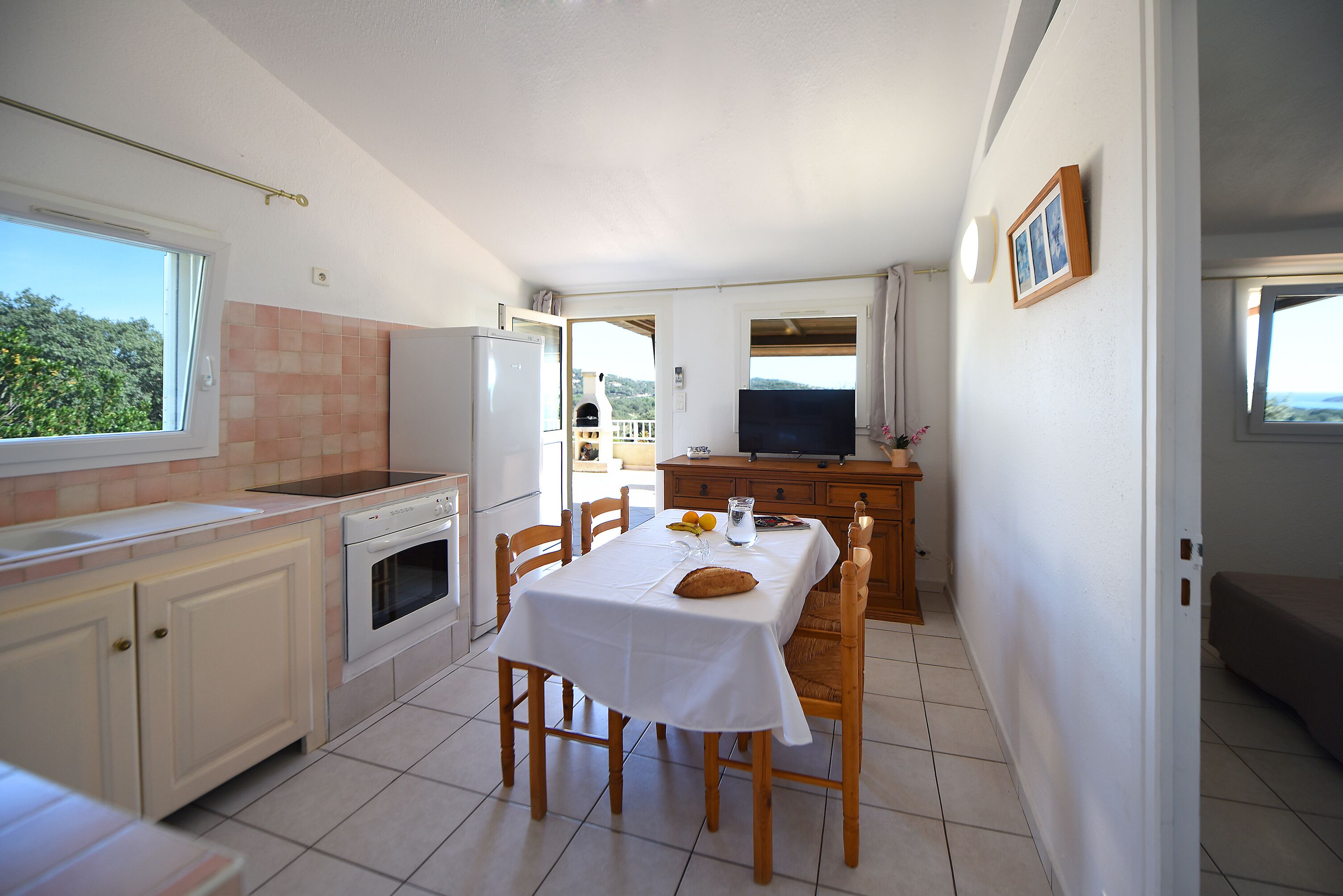 Een keuken met een eettafel, stoelen, een koelkast, oven en een televisie.