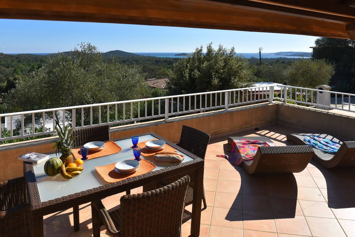 A terrace with a table set for dining, wicker chairs, and a view of the landscape.