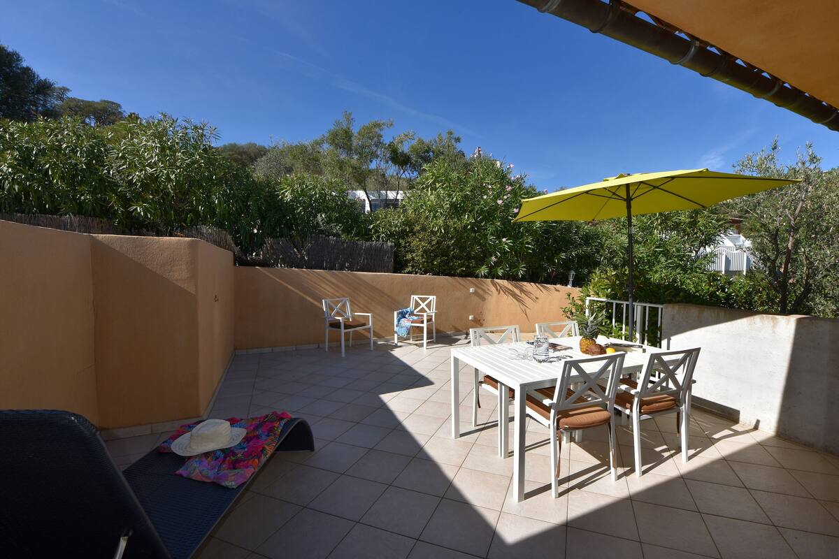 An outdoor patio with a table and chairs, a yellow umbrella, and a hat on the ground.