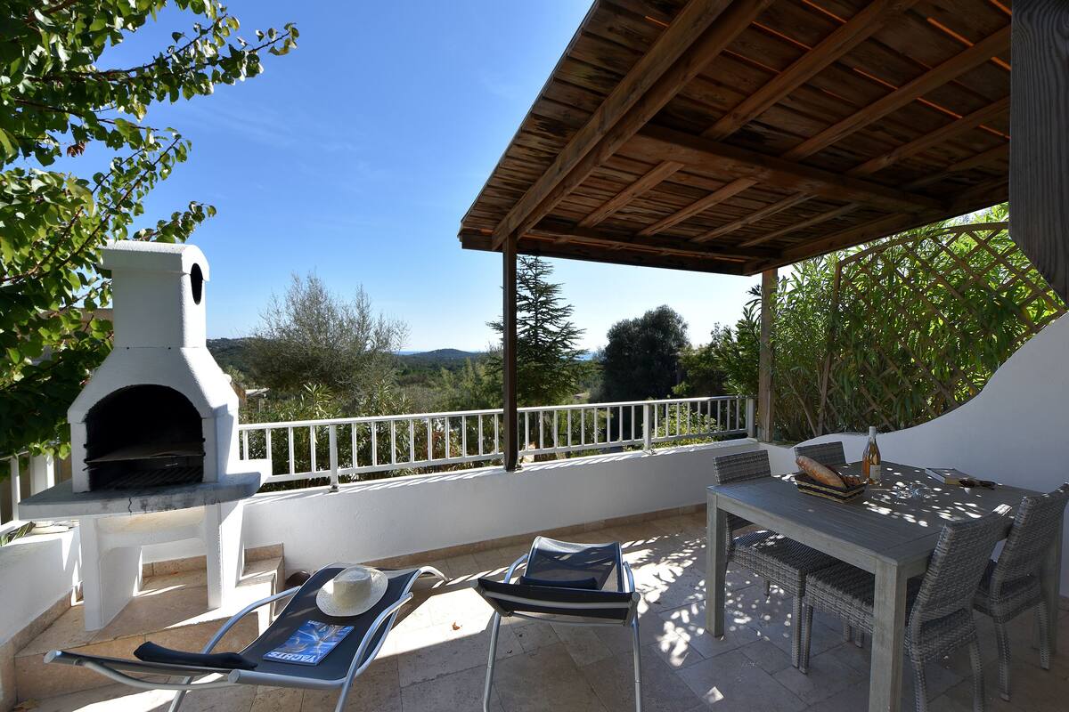 An outdoor patio with a barbecue grill, lounge chairs, and a dining table.