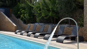 A swimming pool with a water feature, lounge chairs, and a stone wall with stairs leading up. - Résidence Chiar' Di Luna (Zonza)