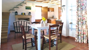 A dining area with a white table and chairs, a fireplace, and a kitchen in the background. - Villa Patmos Netia (Patmos)