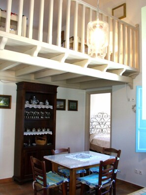Un comedor con una mesa y sillas, un aparador de madera con vajilla, y una escalera con barandilla.
