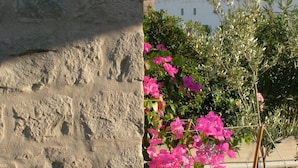 A stone wall with pink flowers in the foreground and a view of a white building and hill in the background. - Villa Patmos Netia (Patmos)