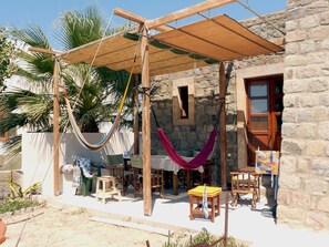 Un área de estar al aire libre rústica con un porche de madera, hamacas y un edificio de piedra con puerta de madera.