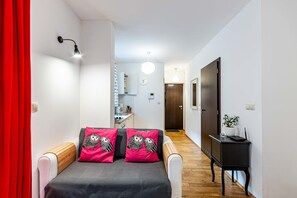 A modern bedroom with a bed, two matching pillows, a bedside table, a wardrobe, and a hallway leading to a kitchen area. - HappyGuests Apartments (Kraków)