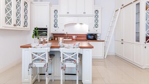 A kitchen with white cabinetry, a wooden countertop, and two white chairs with floral upholstery. - HappyGuests Apartments (Kraków)