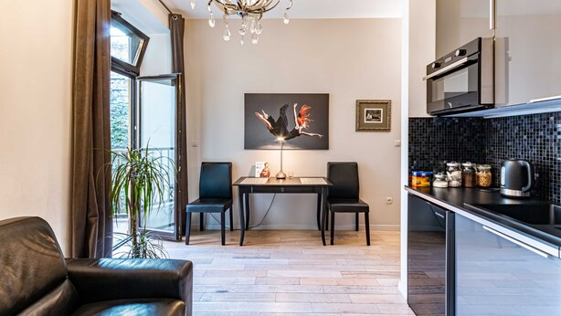 A modern kitchen with a dining area, featuring a chandelier, a dining table with chairs, and a view through a large window. - HappyGuests Apartments (Kraków)