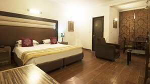 A hotel room with a large bed, a bedside table, a chair, a small table, and a dining area with a chair and table. - Golden Leaf (New Delhi)