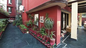 A narrow corridor with potted plants lining the walls, a clock, and a door leading to a room. - Golden Leaf (New Delhi)