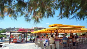 An outdoor bar area with yellow canopies, tables, and chairs. - Sea Side Apartments (Chania)