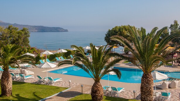 A pool area with lounge chairs and umbrellas, palm trees, and a view of the sea. - Sea Side Apartments (Chania)