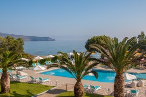 A pool area with lounge chairs and umbrellas, palm trees, and a view of the sea. - Sea Side Apartments (Chania)