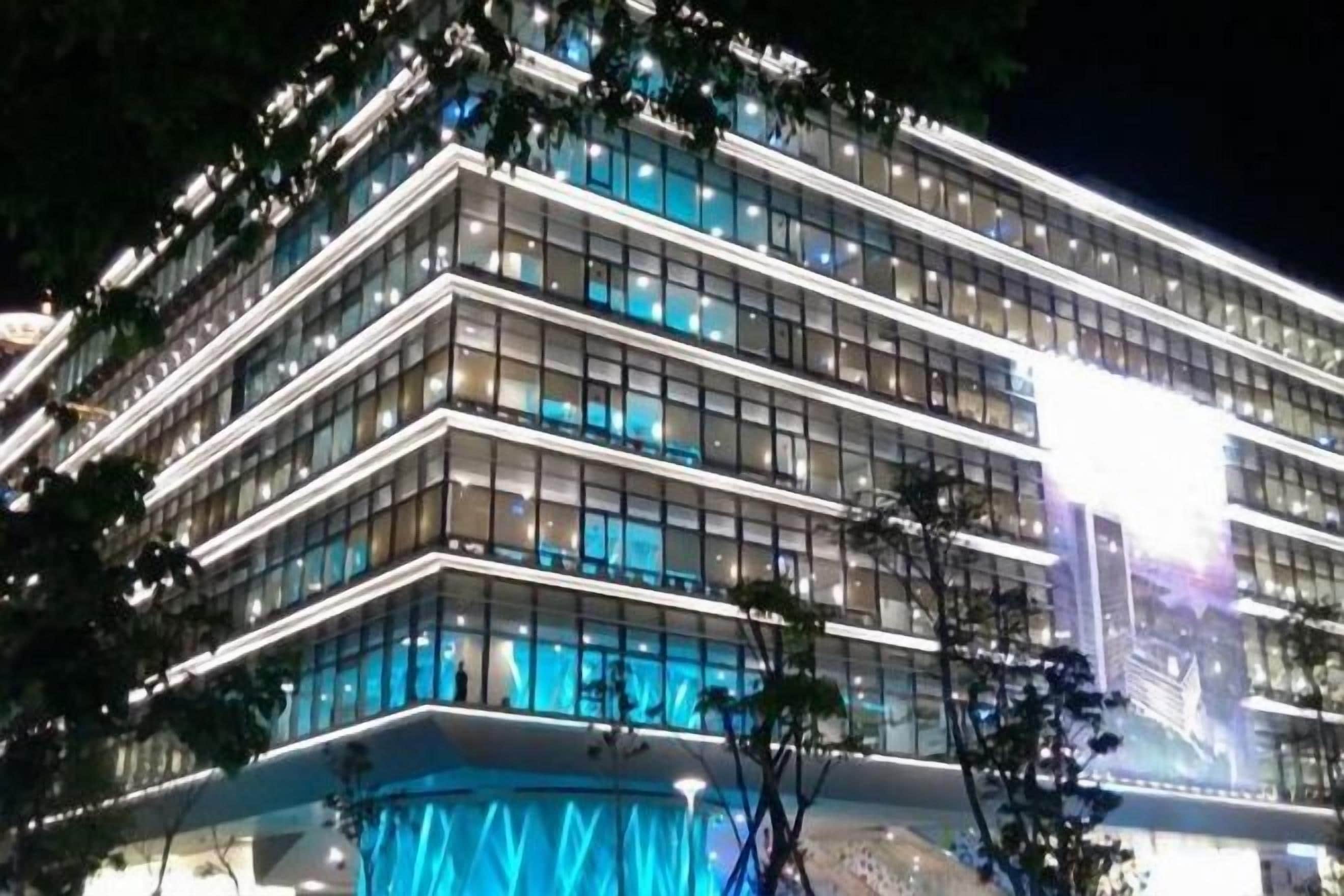 A multi-story building with a modern architectural design, featuring a prominent glass facade and a series of illuminated windows.