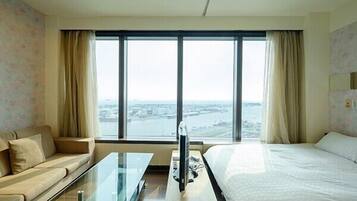 A hotel room with a large window, a sofa, a bed, and a glass coffee table.