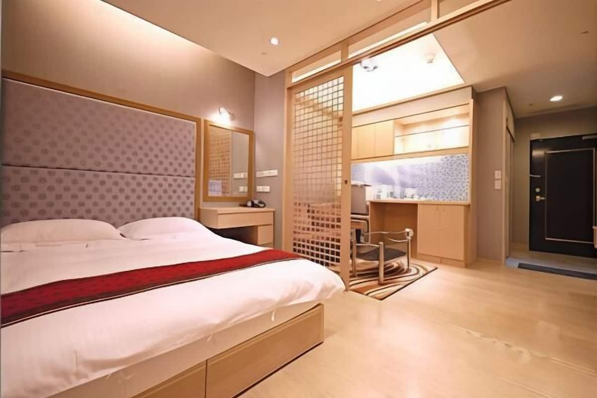 A modern bedroom with a large bed, a wooden wardrobe, a desk, and a mirror.