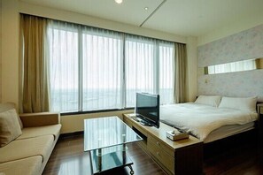 A hotel room with a bed, a sofa, a TV on a desk, and large windows with curtains. - 85 Cape Inn (Kaohsiung)