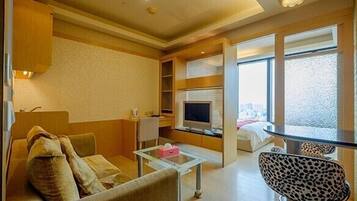 A compact hotel room with a sofa, a glass coffee table, a leopard-print chair, a TV, and a large window offering a city view.