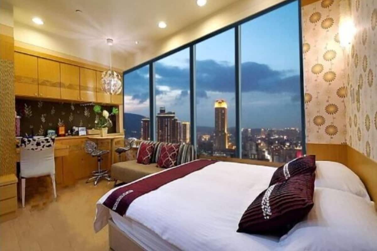 A hotel room with a large bed, a desk, and a view of a cityscape.