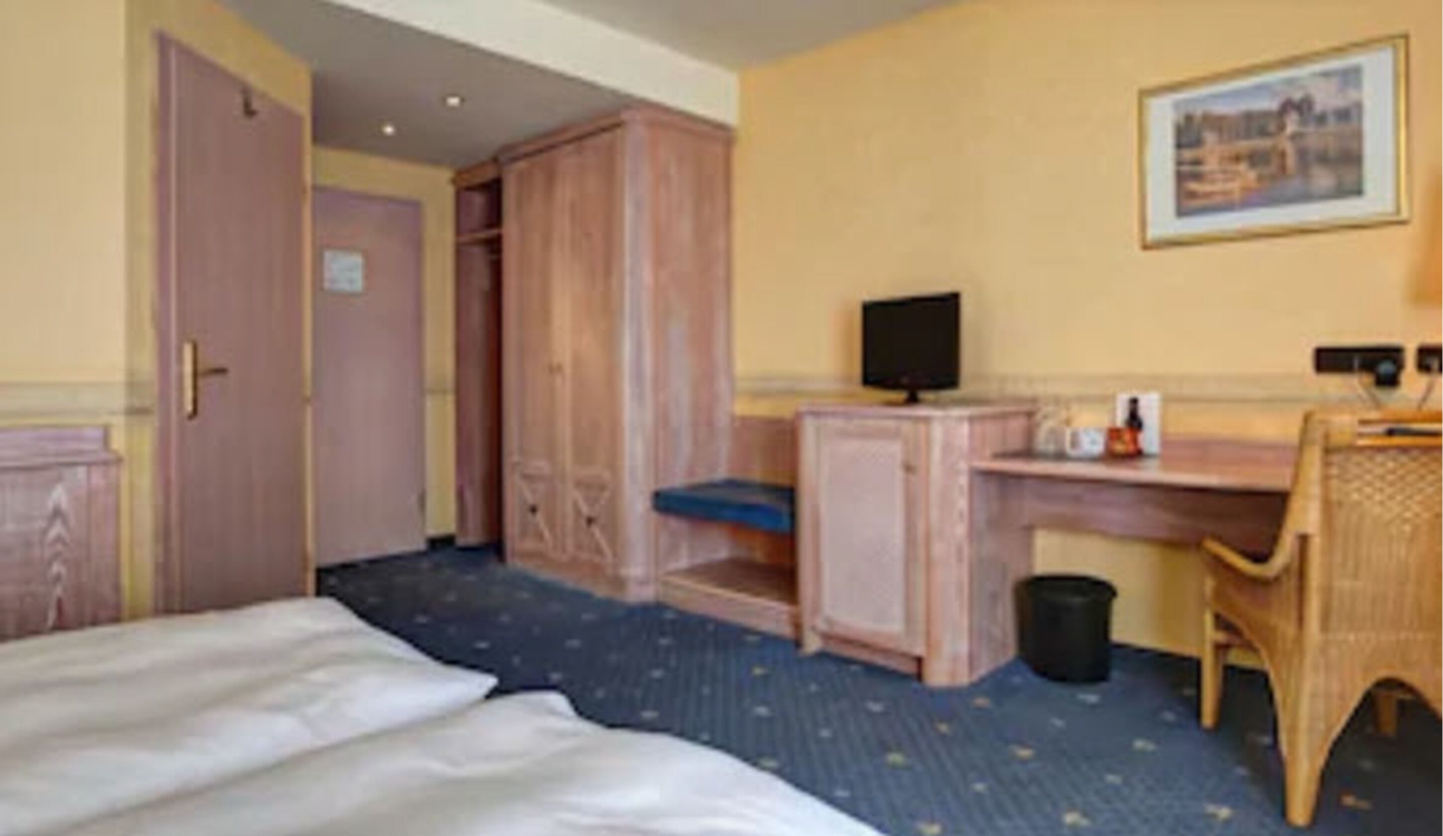 Una habitación de hotel con una cama, un escritorio con una computadora, una silla y un pequeño cesto de basura.