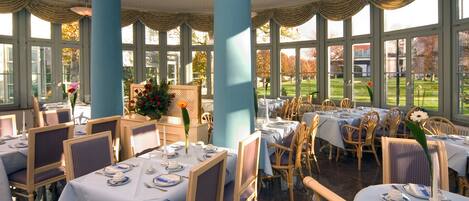 A dining area with tables set for service, large windows, and a view of a lawn.