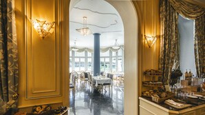 Un corridoio d'albergo con una sala da pranzo sullo sfondo, con lampadari, tavoli e sedie.