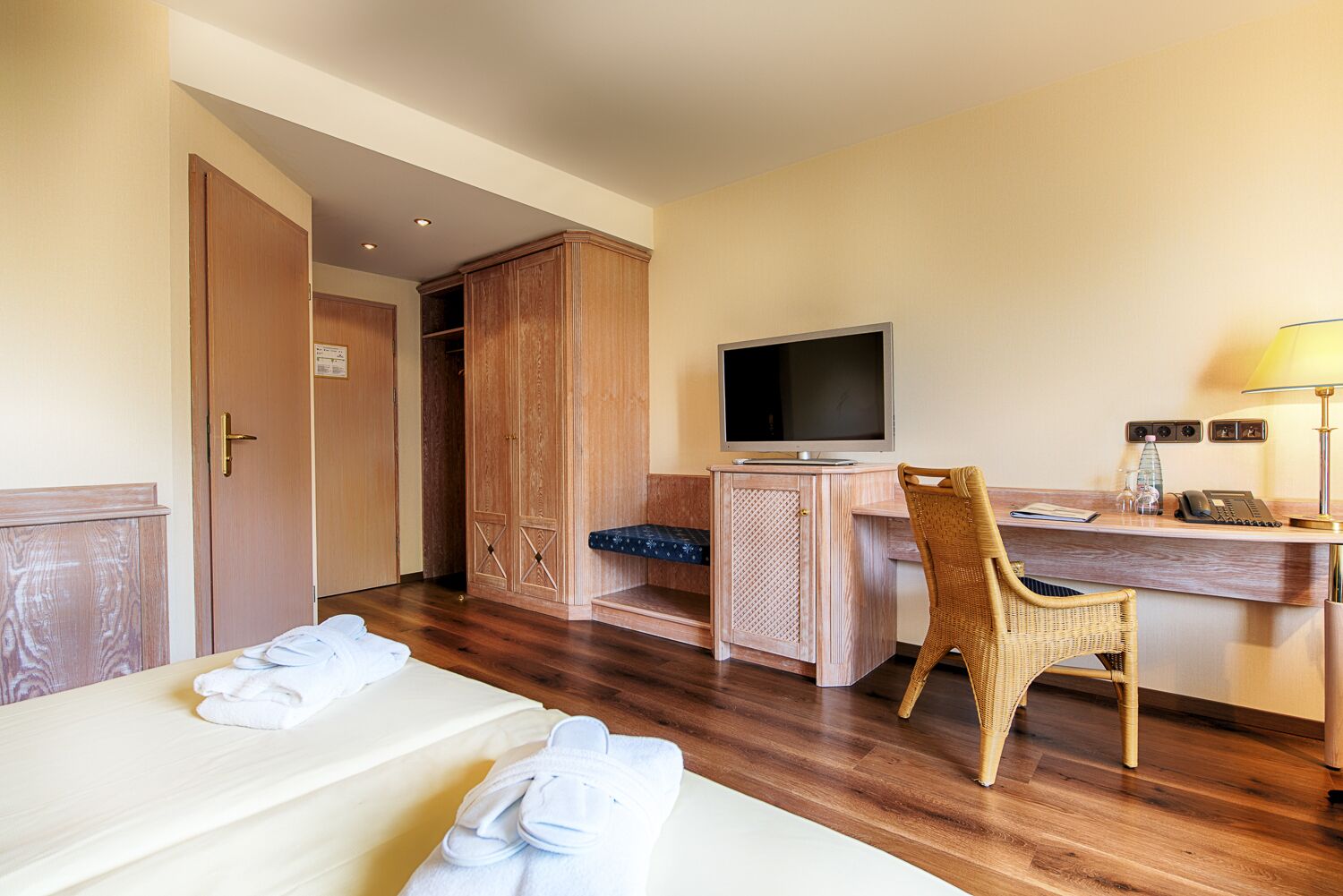 Ein Hotelzimmer mit einem Bett, einem Schreibtisch mit Computer, einem Fernseher, einem Sessel und einem Kleiderschrank.