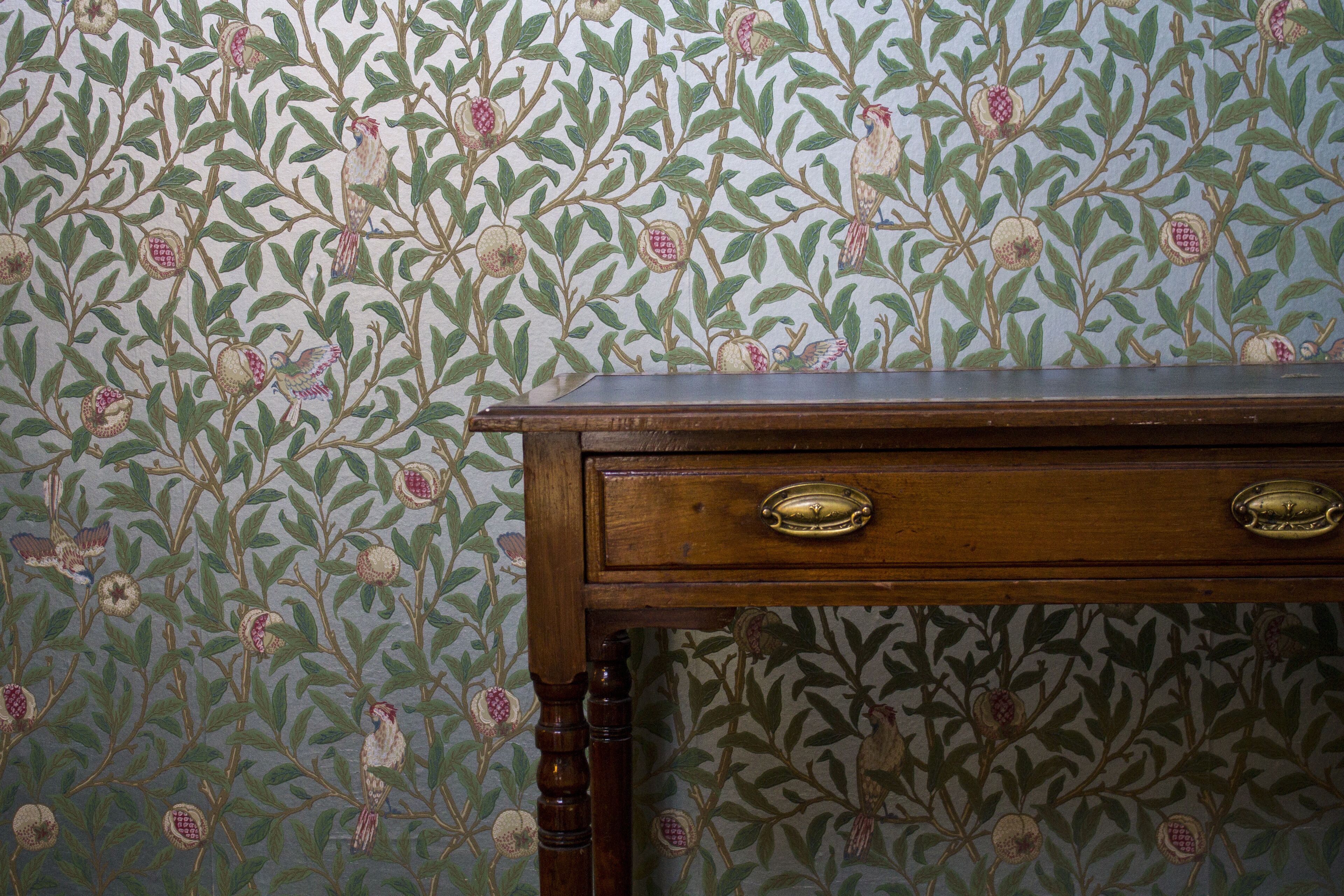 A wooden dresser with two drawers against a wallpapered wall with a floral pattern.