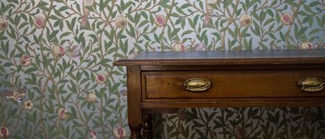 A wooden dresser with two drawers against a wallpapered wall with a floral pattern.