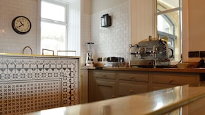 A kitchen with white tiled walls, a clock, a coffee machine, and a window. - The Park Hotel Peebles (Peebles)