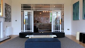A spacious living area with a modern design, featuring a large black sofa, a glass coffee table, and a kitchen visible through glass doors. - The Park Hotel Peebles (Peebles)