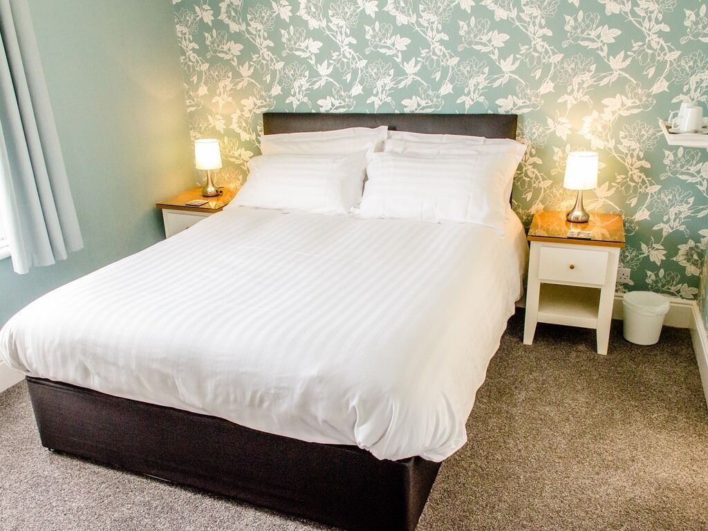 A neatly made bed with white linens, two bedside tables with lamps, and a floral wallpaper pattern.