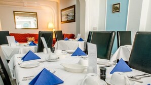 A dining area with tables set for service, featuring blue napkins, white tablecloths, and black chairs. - The Avenue (Shanklin)