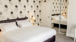 A neatly made bed with white linens, a dark headboard, and a bedside lamp on a nightstand. - The Avenue (Shanklin)
